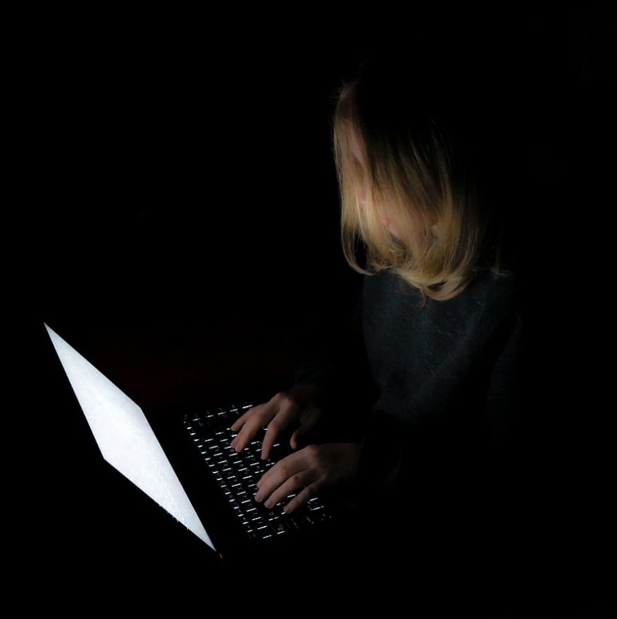 A girl stares at her screen in the dark, straining her eyes as she types.