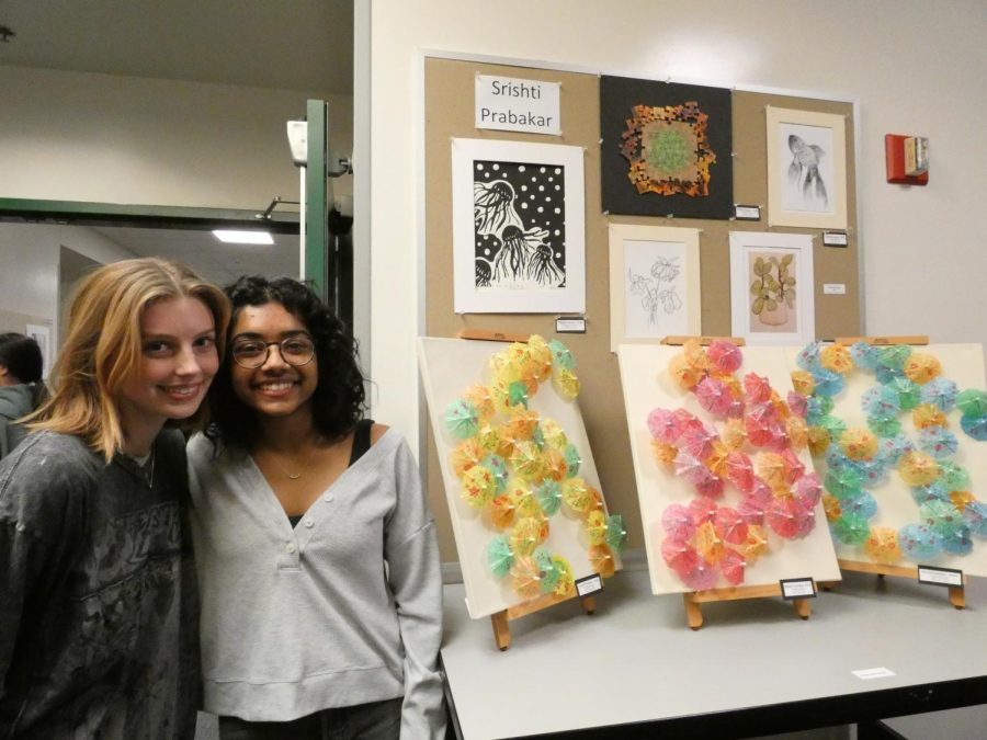 Senior art students Emma Blevens and Srishti Prakabar smile in front of Prakabar’s art display at the show.