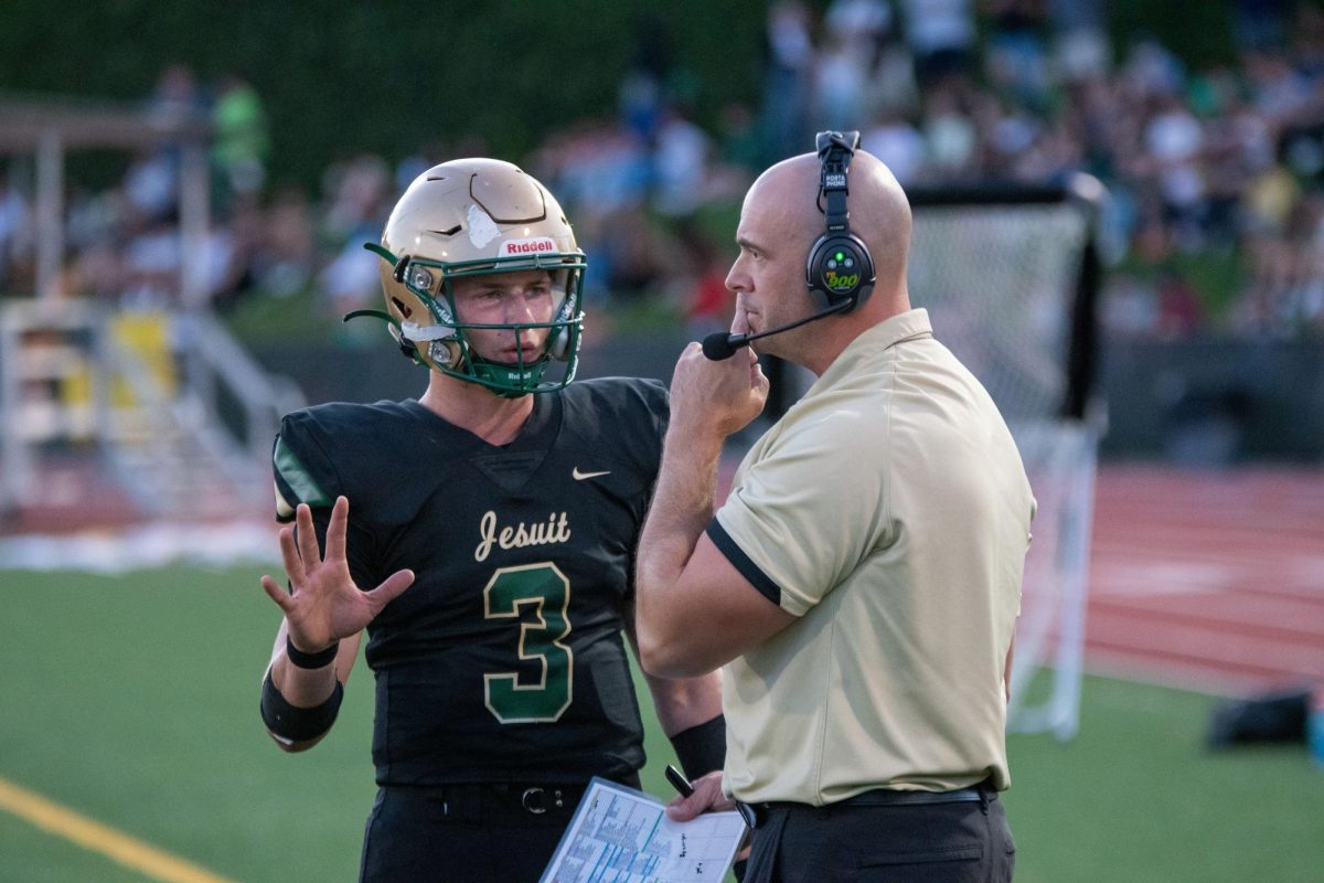 Varsity assistant coach John Andreas speaks with quarterback Treynor Cleeland during the game. 