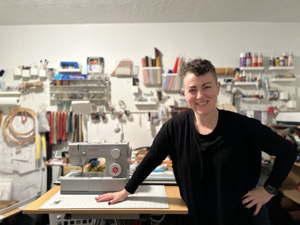 Ms. Schick stands in front of her home studio, surrounded by craft supplies, tools, and machines.